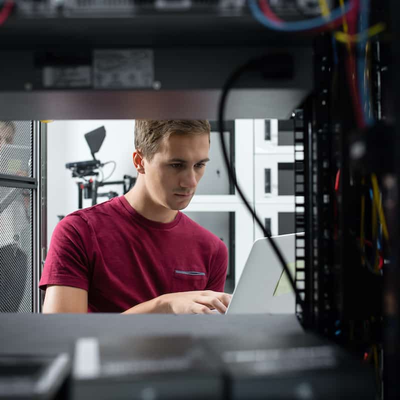 Male server engineer working of a laptop in a large data centre.