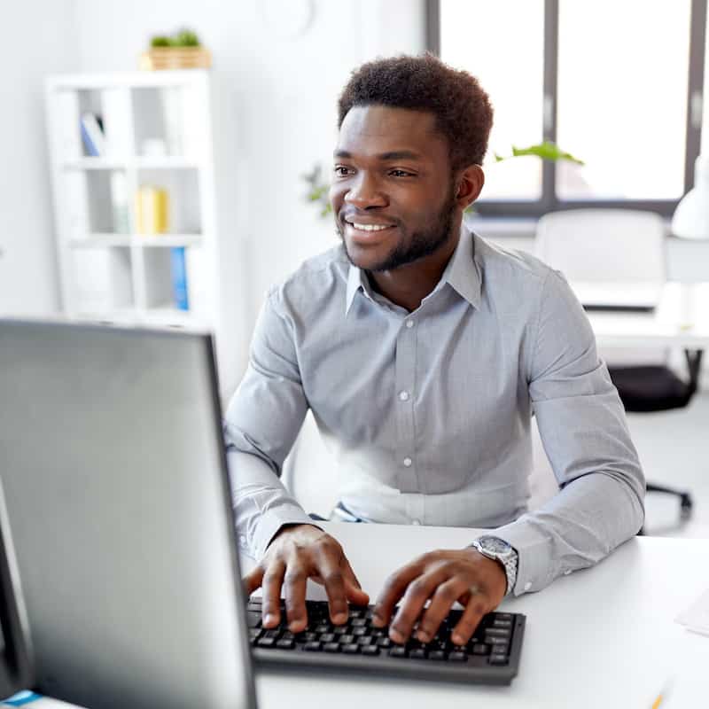 African-American businessman smiling working on a computer at an office.