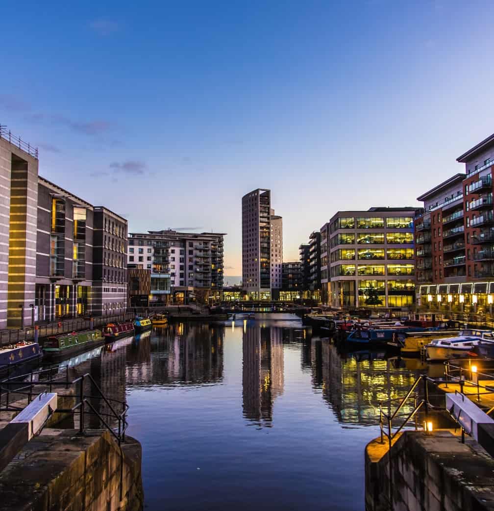 Image of a city centre with high ride buildings surrounding a body of water with barges on.