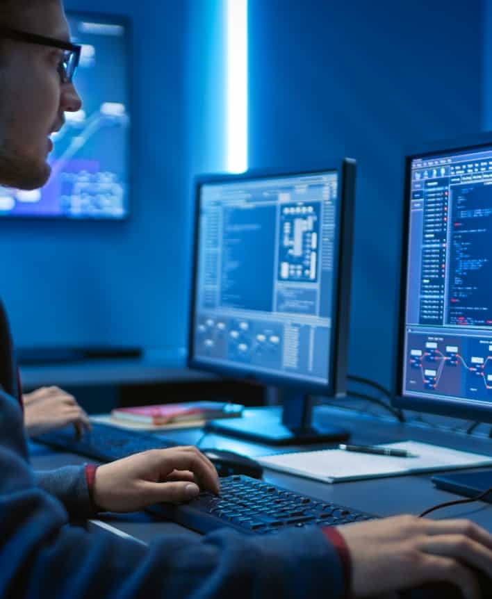 Male data analyst sat at a desk looking at data and graphs on a computer screen.